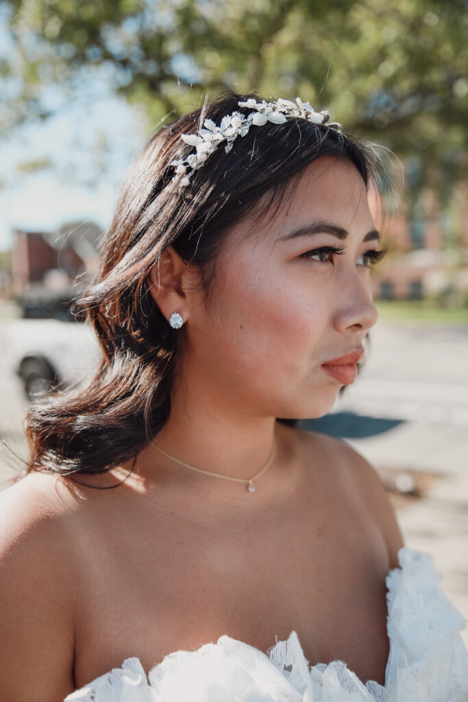 Bride wearing a delicate, floral headband with pearl accents and subtle stud earrings, captured in natural outdoor lighting.