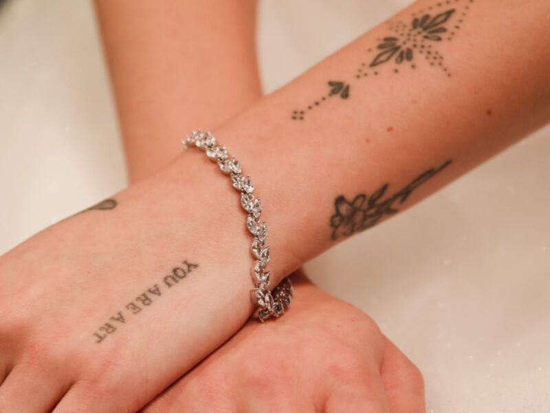 Close-up of hands with tattoos, adorned with a sparkling diamond bracelet, showing intricate bracelet design details.