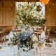 A rustic wedding setup with tables featuring soft blue and white florals in a barn with warm natural wood tones.