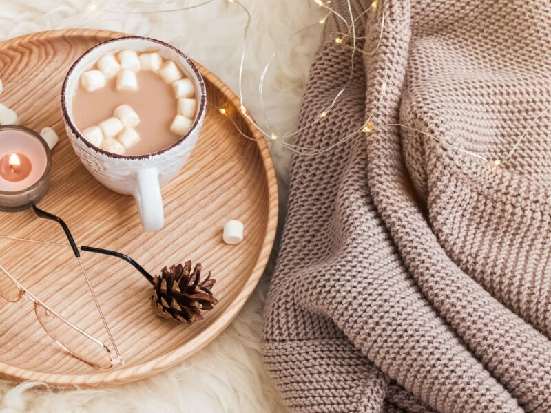 A wooden tray featuring hot cocoa with marshmallows, pinecones, and a candle, evoking warmth and charm for a winter reception.