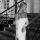 A black-and-white image captures a bride gracefully descending a staircase in a fitted wedding gown with lace sleeves.