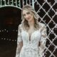 A bride smiles gracefully in a fitted lace gown with a sheer neckline, illuminated by twinkling fairy lights in a nighttime garden.