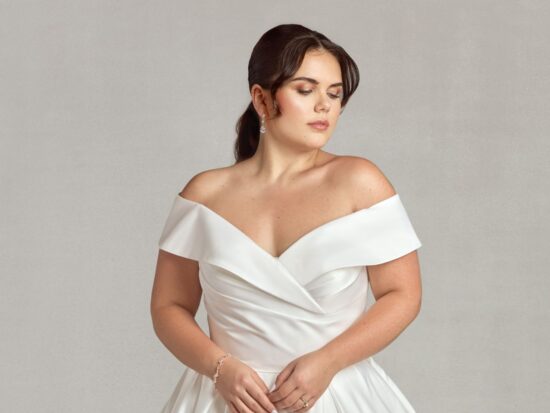 A bride wearing an elegant off-the-shoulder satin wedding dress with a fitted bodice and a flowing skirt, showcasing timeless sophistication.