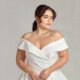 A bride wearing an elegant off-the-shoulder satin wedding dress with a fitted bodice and a flowing skirt, showcasing timeless sophistication.