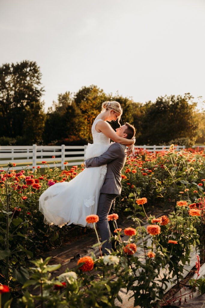 Groom lifting his bride and spinning her around in a field of wildflowers.