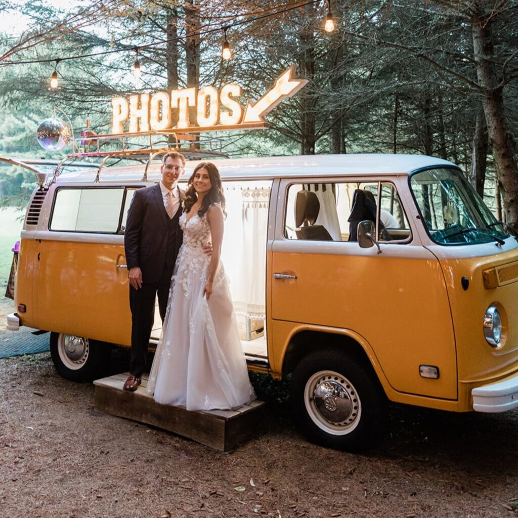 Bride and Groom standing in front of an antique Volkswagon bus in the woods.