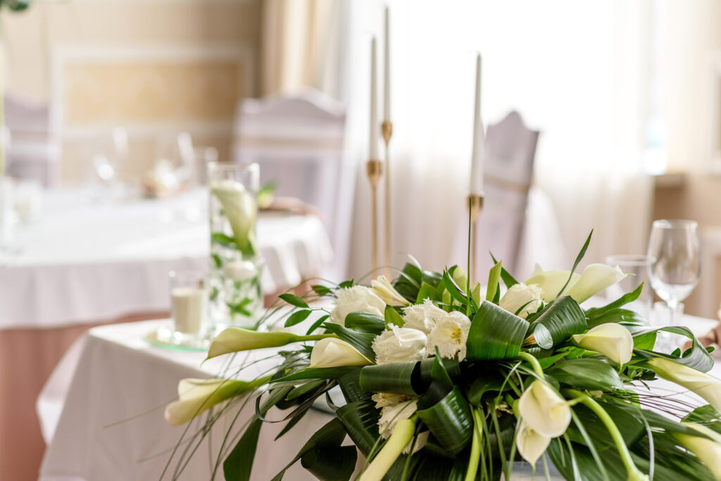 Sophisticated wedding centerpiece with white calla lilies and lush greenery, paired with tall gold taper candles and clear glassware on elegant tables.