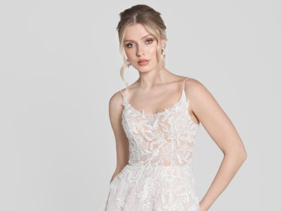 A model wears a romantic A-line wedding dress with a sheer, lace-adorned bodice and delicate spaghetti straps.
