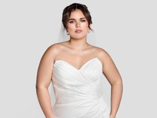 A close-up of the same bride wearing a strapless ruched gown and veil, with soft makeup and drop earrings.