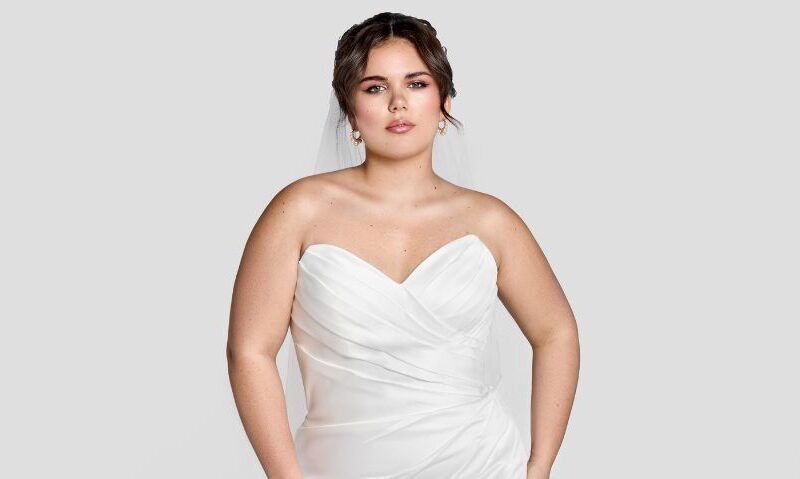 A close-up of the same bride wearing a strapless ruched gown and veil, with soft makeup and drop earrings.