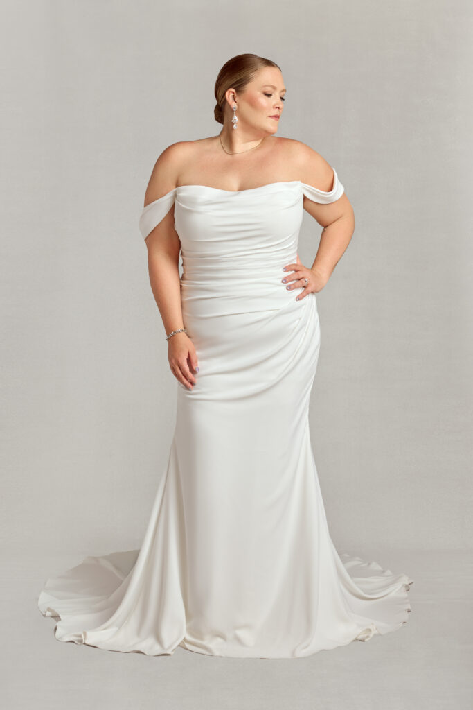 Plus-size bride wearing an off-the-shoulder ruched crepe gown with a flattering fit and flare silhouette.