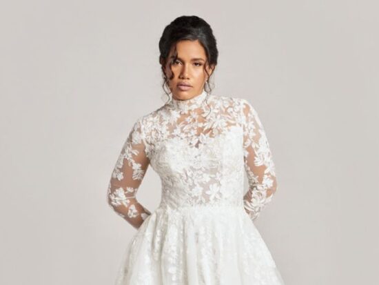 A close-up of a bride in a high-neck lace wedding dress with long illusion sleeves and a floral applique bodice, highlighting the intricate texture and romantic style.