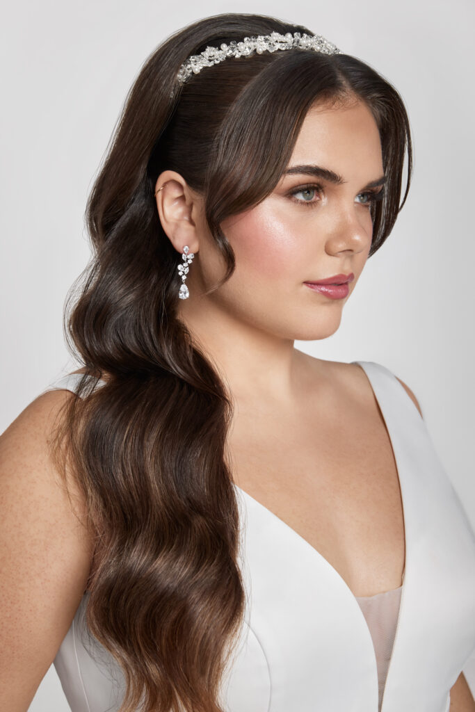 A close-up of a bride wearing a sparkly headband and drop earrings with long, wavy hair and natural makeup.