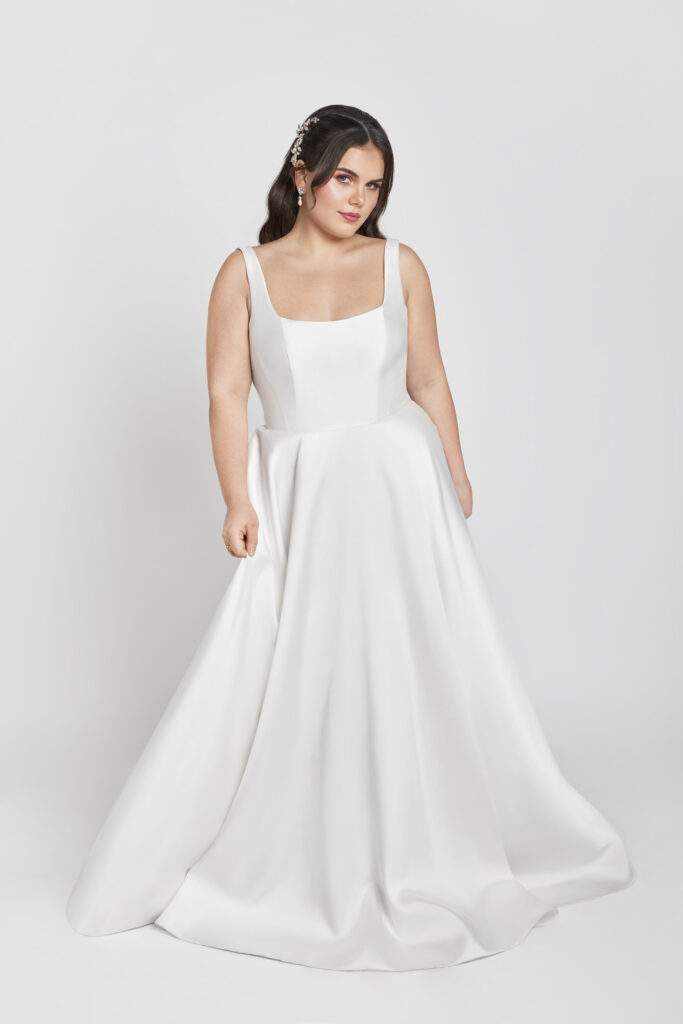 A bride in a sleeveless square-neck satin wedding gown with a full A-line skirt, posing against a light gray background.