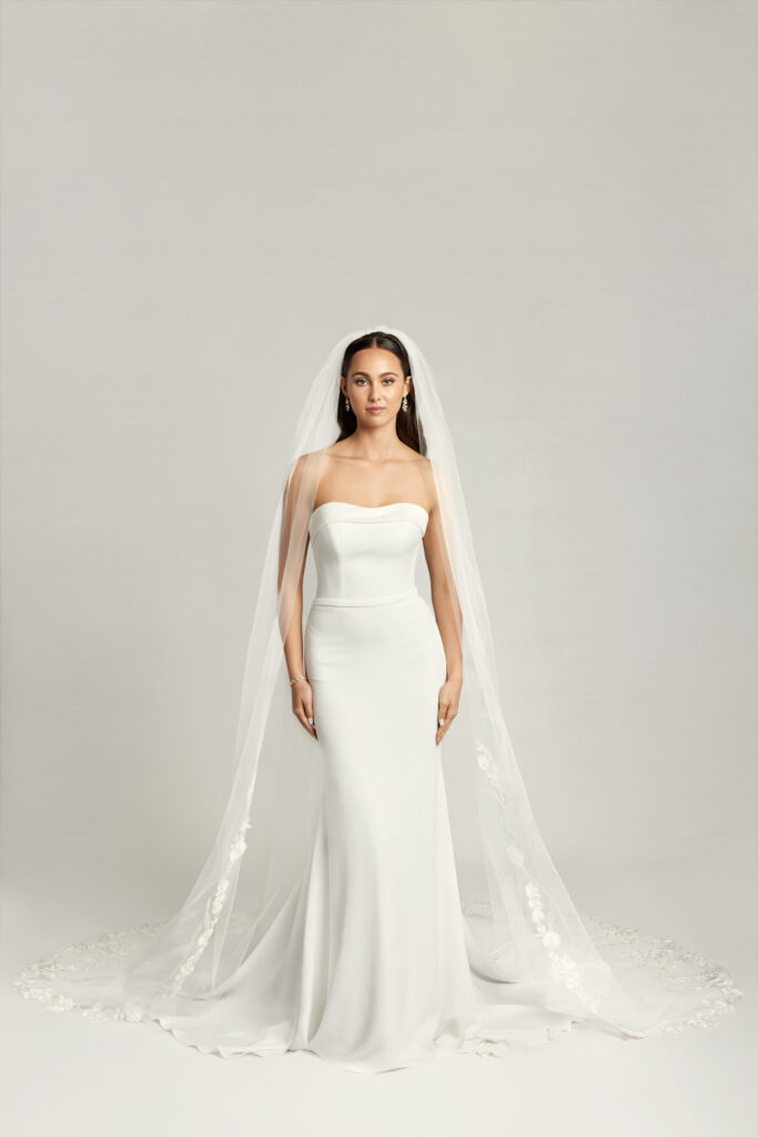 Bride in a strapless crepe wedding dress with a cathedral-length veil and a minimal, elegant silhouette.