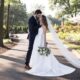 Bride and groom in garden setting, bride in a floral lace dress holding a pastel bouquet, groom in a black tuxedo.