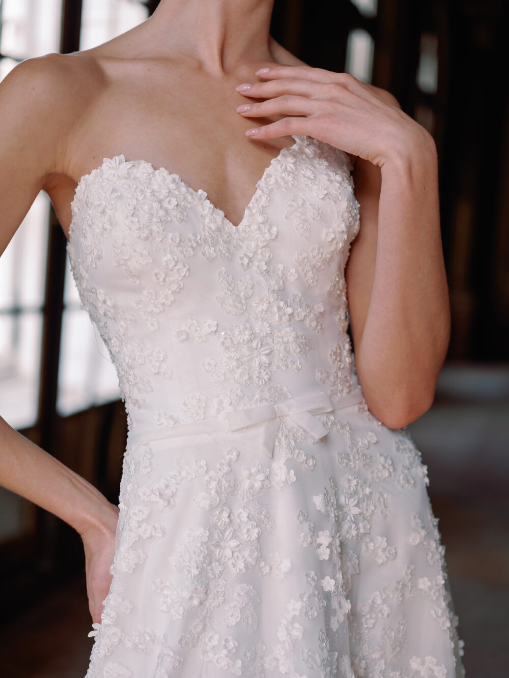 A bride wears a strapless Sareh Nouri gown with floral lace appliqués and a delicate bow at the waist.