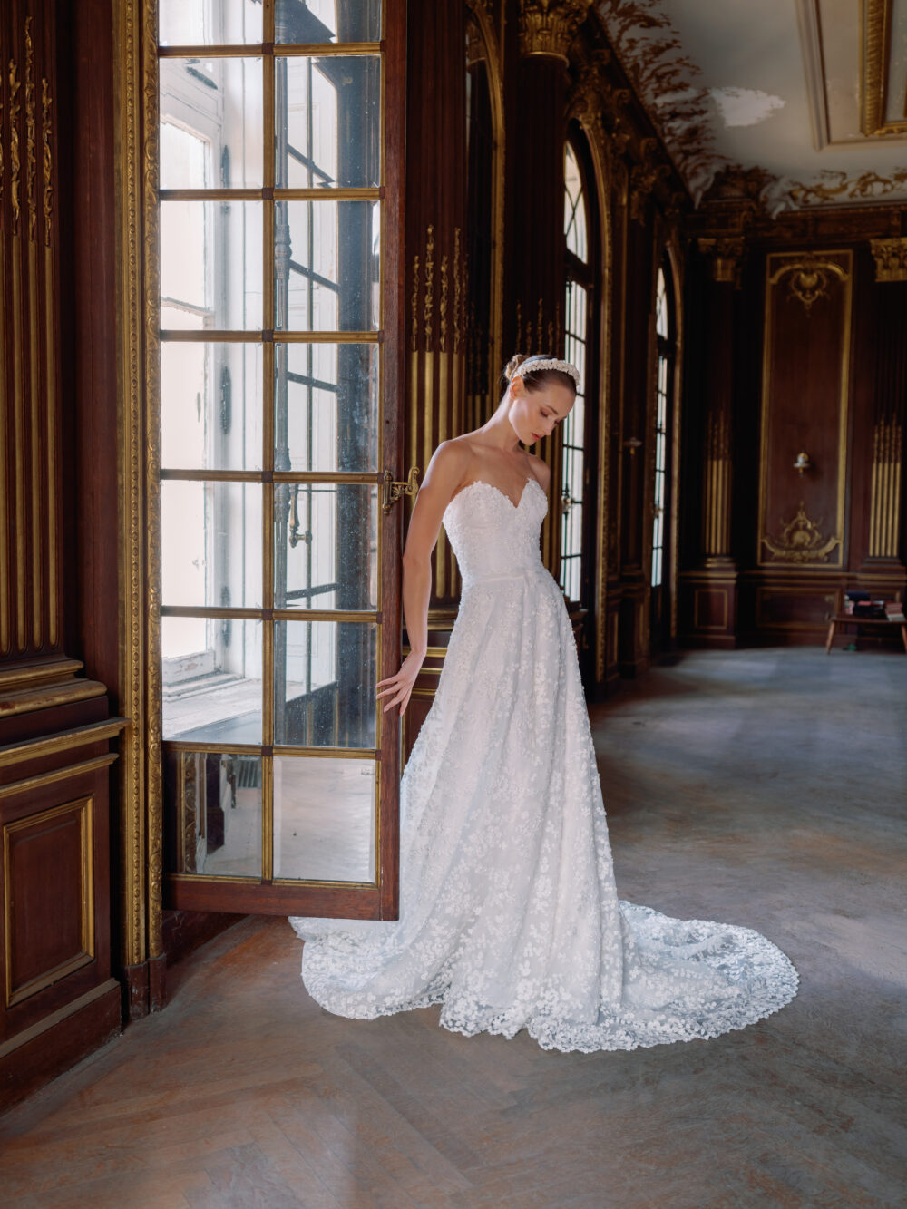 A bride poses in a strapless floral lace Sareh Nouri gown while standing in an ornate ballroom doorway.