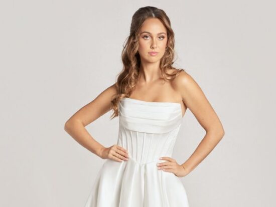 A studio image of a model wearing a strapless white corset wedding dress with a pleated satin bodice and flowing ballgown silhouette.