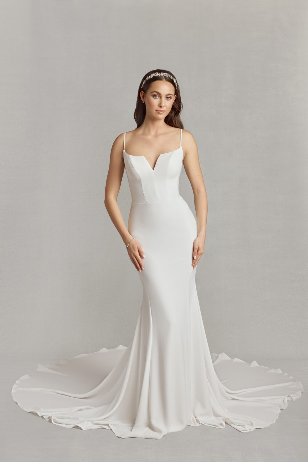 Bride in a fitted minimalist gown with a deep V neckline and delicate straps, standing gracefully with a long train.