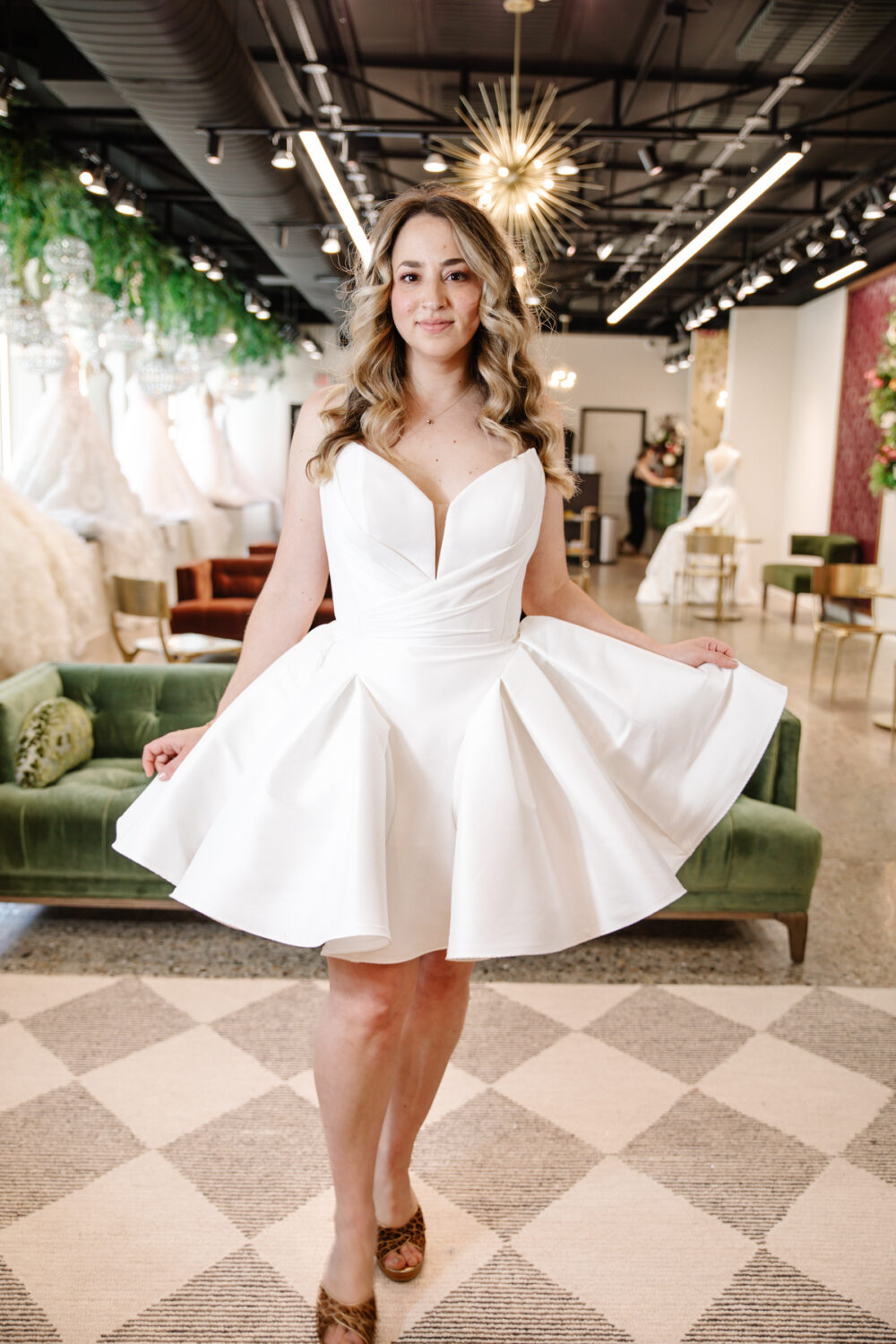 A smiling bride twirls in a short strapless wedding dress with a structured sweetheart neckline and full pleated skirt at The Wedding Shoppe.