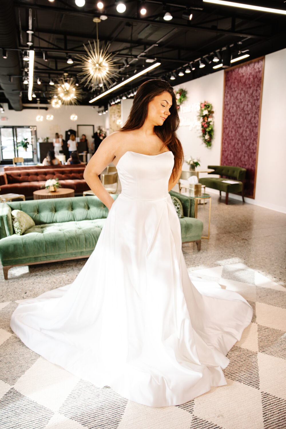 Bride posing inside a bridal boutique in a strapless A-line wedding gown with a softly curved neckline and subtle train.