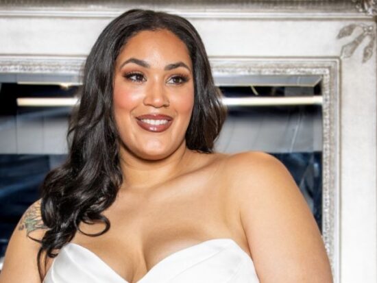 Close-up of a smiling bride in a sweetheart neckline wedding gown, standing in front of an ornate silver mirror.