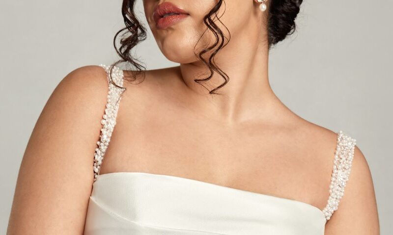 The image highlights the bride’s beaded straps and soft curls, framing her shoulders and the top of her structured square neckline wedding dress.