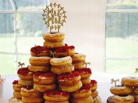 A donut tower with red velvet and glazed donuts, topped with a “Mr & Mrs” sign at a wedding.