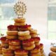 A donut tower with red velvet and glazed donuts, topped with a “Mr & Mrs” sign at a wedding.