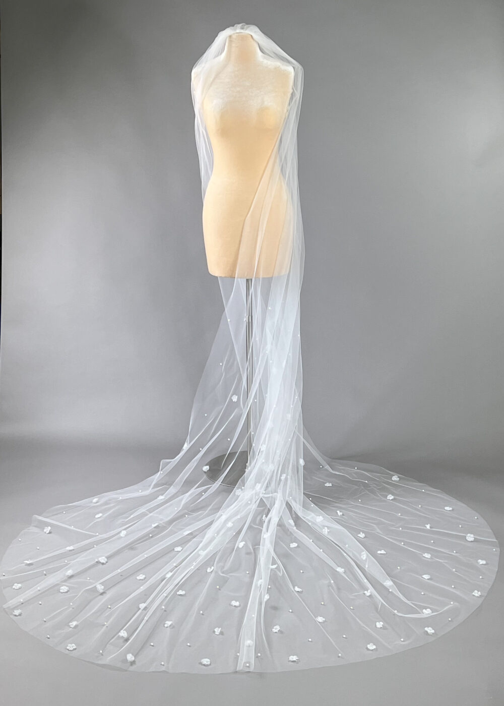 A long cathedral wedding veil with floral appliqués and pearls cascades gracefully over a mannequin.