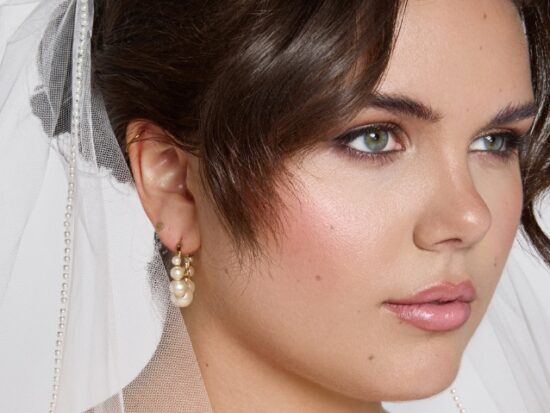 A bride wears a pearl-trimmed wedding veil, paired with drop pearl earrings and soft romantic makeup.