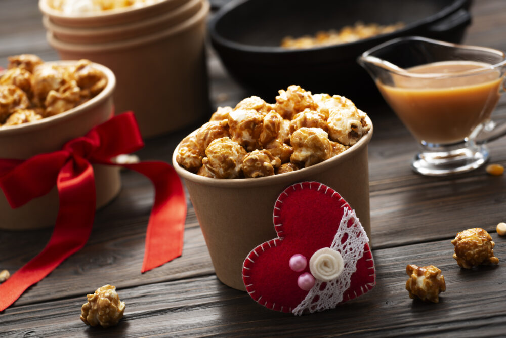Caramel popcorn served in brown paper cups, decorated with red bows and heart embellishments.