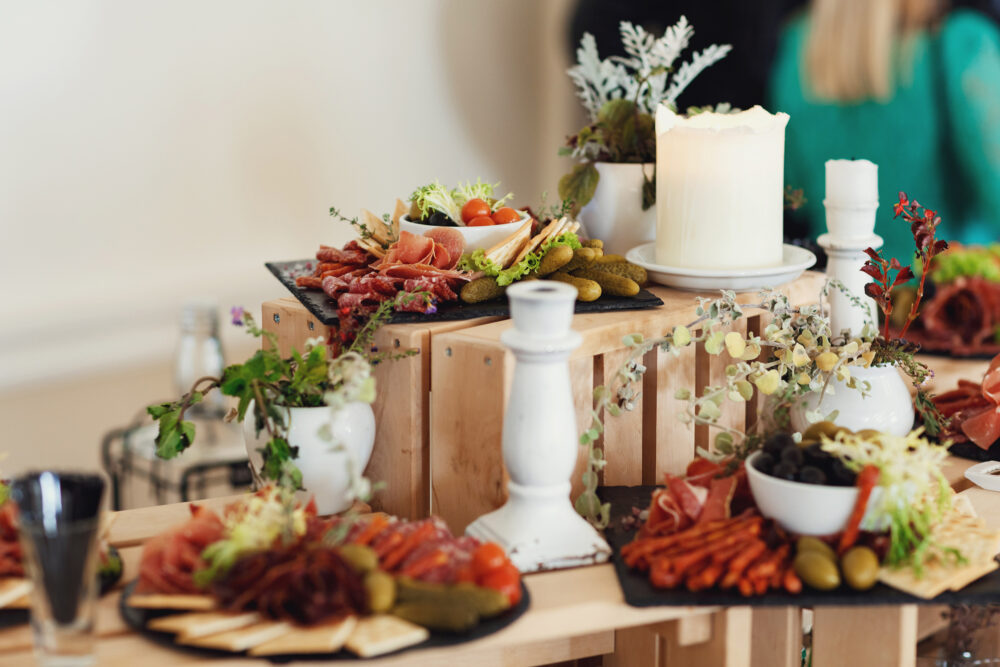 Rustic charcuterie display with meats, cheeses, pickles, and greenery on wood crates and slate boards.