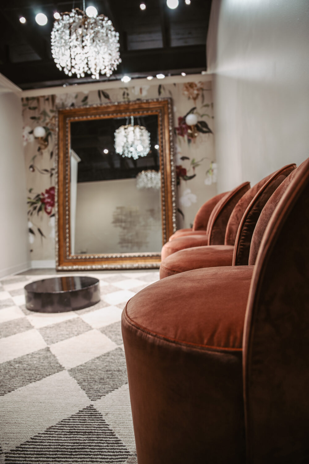 Close-up of rust velvet chairs and a large ornate mirror in a stylish bridal fitting room with floral wallpaper.