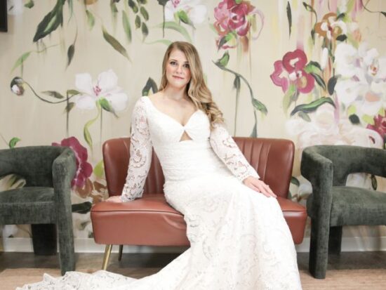 A bride lounges on a pink velvet couch wearing a long-sleeved lace wedding dress with a sweetheart neckline and a small front cutout.
