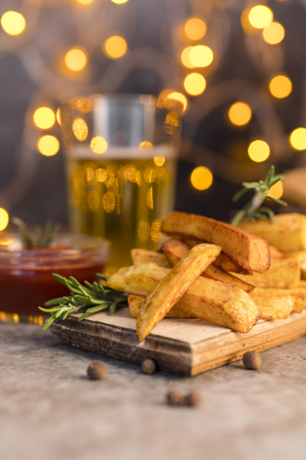 Golden French fries served with rosemary garnish and dipping sauce, with festive lights in the background.