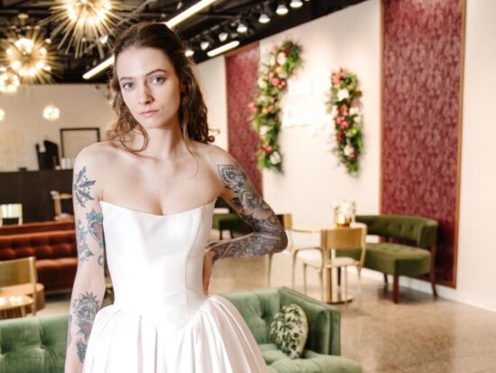 A model in a bridal boutique wears a strapless satin gown with a sculpted neckline and visible corset detailing.