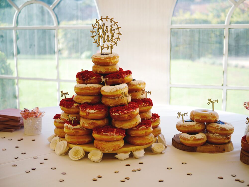 Wedding donut display featuring red velvet and powdered donuts arranged in towers on a white tablecloth.