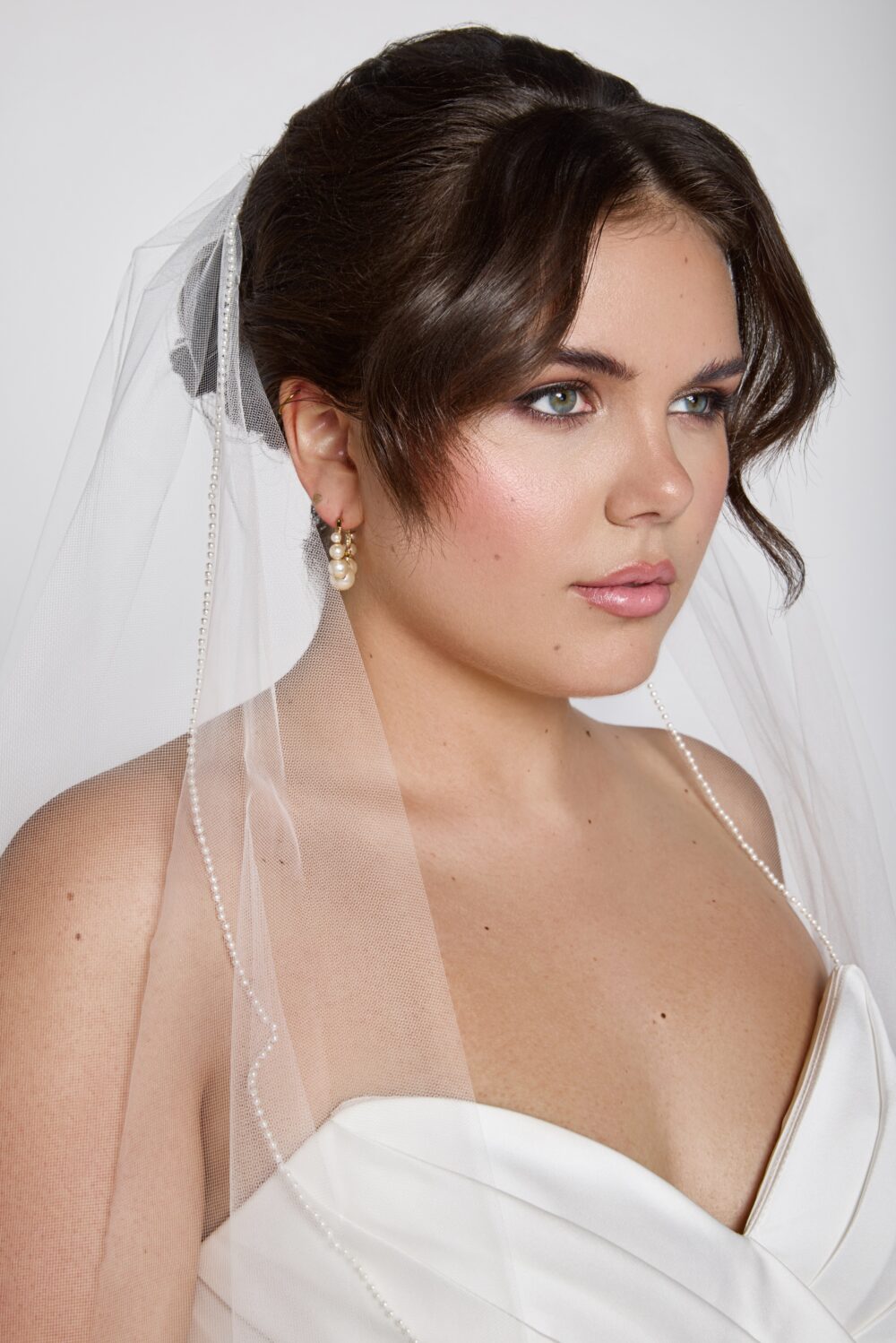 A close-up shows a bride wearing a pearl-trimmed veil draped over her shoulders and soft updo hairstyle.
