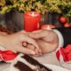 A close-up shot captures the bride and groom gently holding hands on the table next to a slice of chocolate cake and red candles.