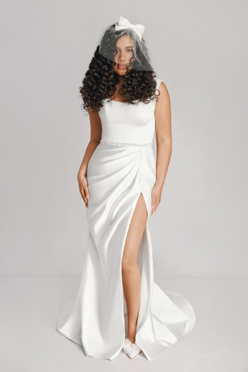 A bride in a white fitted dress with leg slit with a bow and a bridal veil.