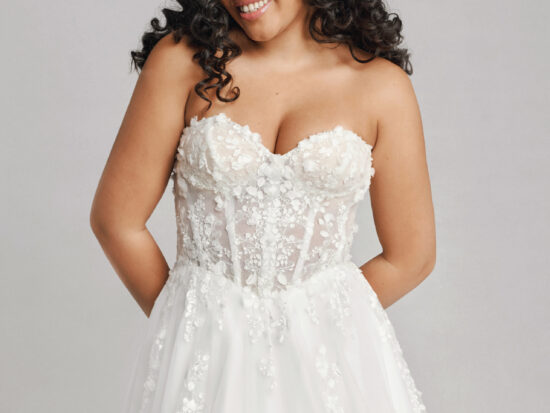 A bride in a white fitted strapless floral lace dress.