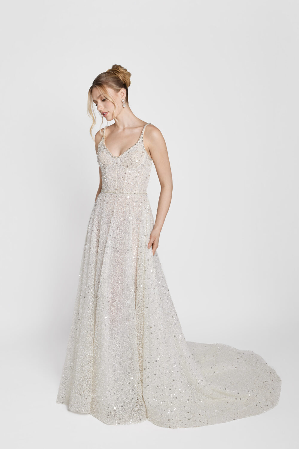 Bride wearing a sparkly, silver-sequined A-line gown with thin straps and a flowing train, looking down with her hands at her sides.