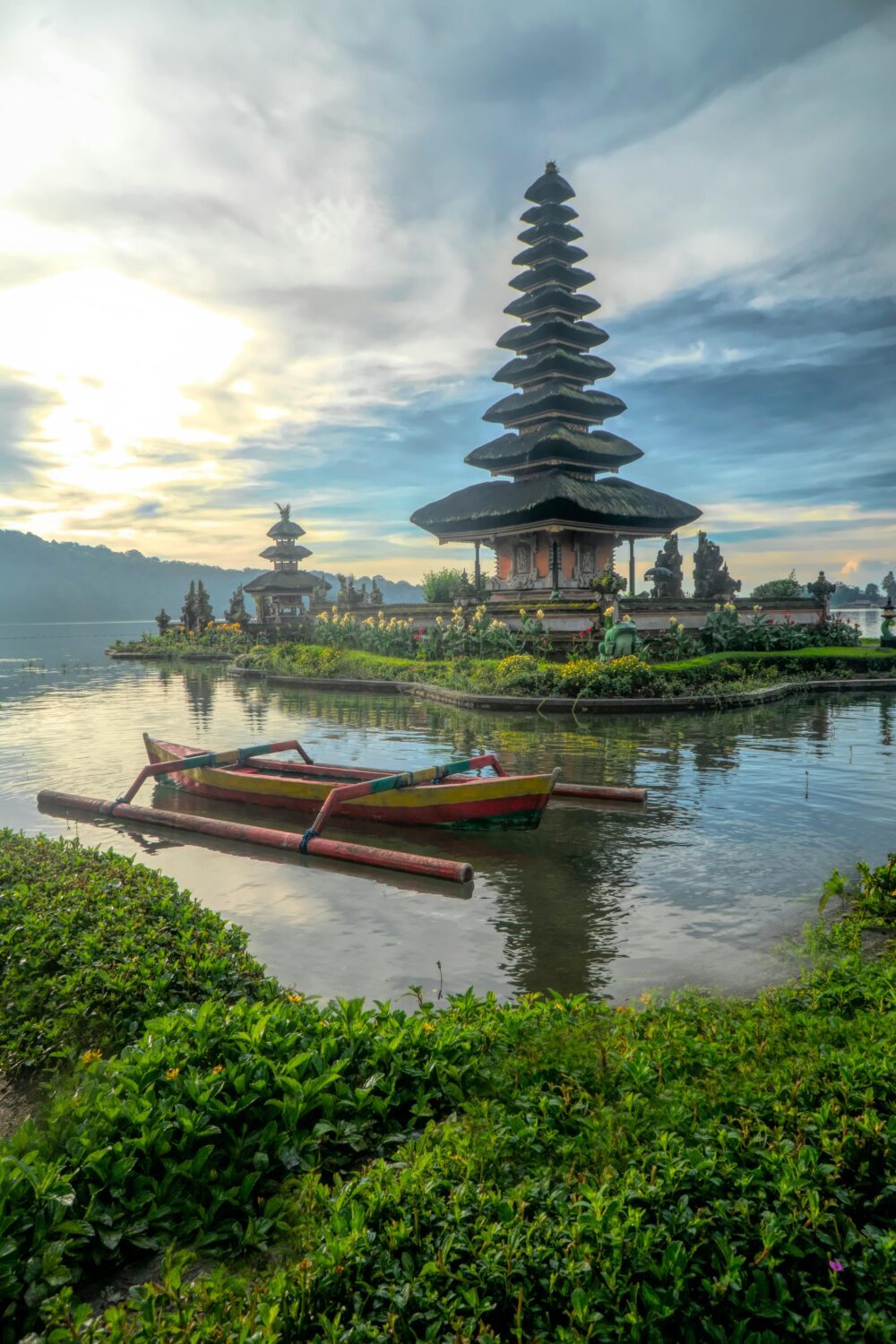 Traditional multi-tiered pagoda-style temple on a small island in a lake with a colorful wooden boat in the foreground.