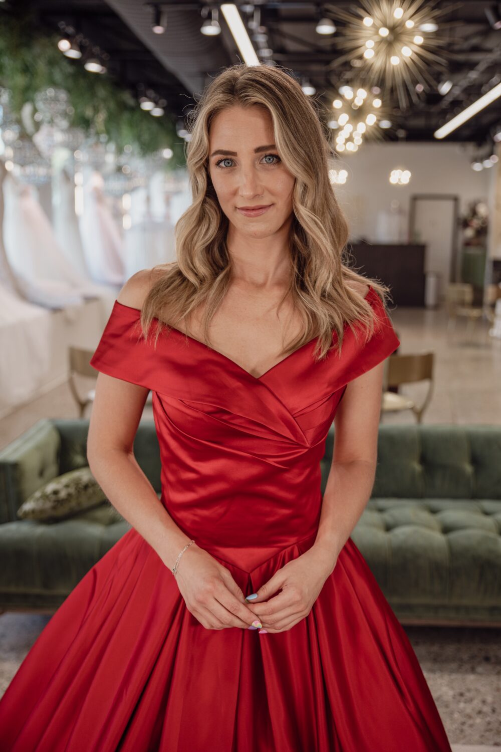 Close-up of a woman in a red satin off-the-shoulder gown standing in a bridal shop.