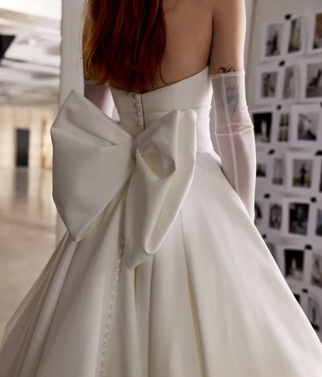 Back view of a strapless wedding gown with a large bow and button detailing down the skirt.