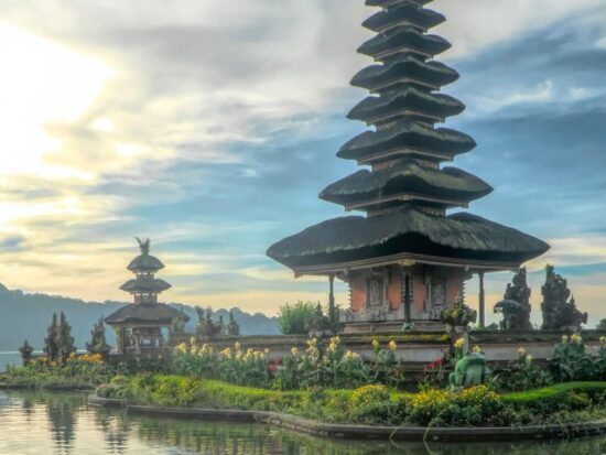 A temple on an island off the shore with the sun rising on the horizon in the background.