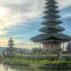 A temple on an island off the shore with the sun rising on the horizon in the background.