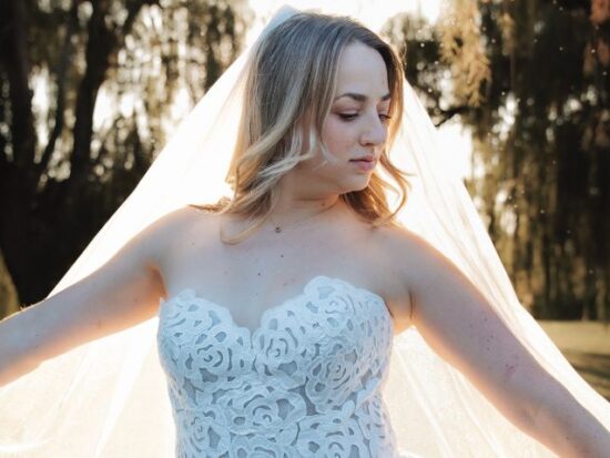 A close-up of a bride in a strapless lace gown with her veil glowing in the sunlight.